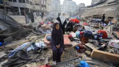 Uma mulher palestina está sentada em meio aos escombros enquanto pessoas inspecionam o local de um ataque israelense em Gaza, em 30 de julho de 2026