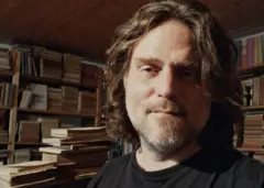 Um homem em primeiro plano com livros atrás.
