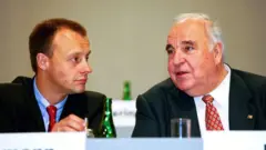 Friedrich Merz de gravata azul à esquerda ouve o velho Helmut Kohl falando