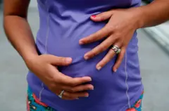 Mulher grávida vestida com top roxo segura sua barriga