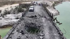 Hürmüzgan vilayetindeki bir köprüde açılan koca delik görünüyor. Geride iki araç ve 10 kadar kişi var. 