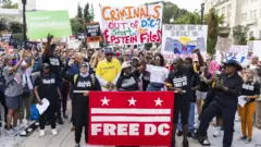 Manifestantes vestidos com camisetas prestas em que se lê "Freedom DC" seguram cartazes pedindo a saída de Trump e a liberdade para a capital dos EUA.