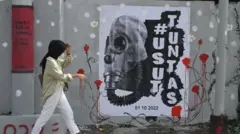 Pejalan kaki melintasi mural bertema tragedi Kanjuruhan di Jalan Simpang Gajayana, Malang, Jawa Timur, Jumat (14/10/2022).