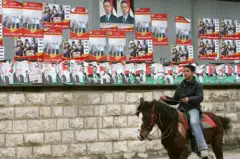 Garoto sobre um cavalo, com cartazes de campanha política ao fundo