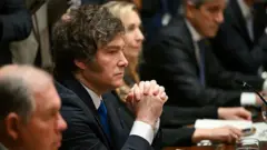 Milei sentado com os braços sobre a mesa e olhar compenetrado durante reunião