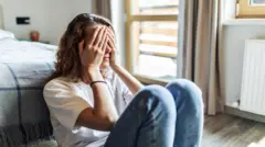 امرأة تغطي وجهها بيديها وتجلس على الأرض 