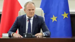 Дональд Туск за мікрофоном на тлі прапорів Польщі та ЄС