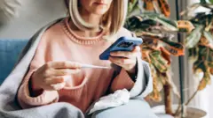 یوه ناروغه ښځه په کور کې ناسته ده، پر اوږو یې کمپله اچولې، ترمامیټر او موبایل ورسره دی او طبي مشورې پکې پلټي.