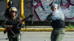 Agentes da Guarda Nacional Bolivariana vestidos de verde e usando capacetes disparam suas armas