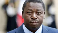 Faure Gnassingbé aganira n'abanyamakuru nyuma y'inama na Perezida w'Ubufaransa i Paris mu mwaka wa 2013. Yambaye ikositimu y'ubururu, n'ishati na karuvati. 