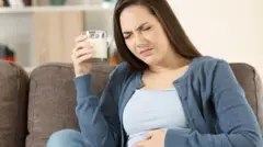 এক হাতে দুধের গ্লাস নিয়ে আরেক হাতে পেট ধরে বসে আছেন এক নারী