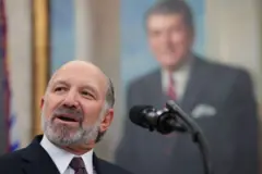 Secretário de Comércio Howard Lutnick, um homem branco idoso, de barba branca, ficando alvo, em frente a uma foto de Ronald Reagan