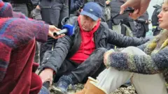 Milan Knežević sedi na zemlji zajedno sa drugim demonstrantima