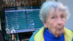 Mujer ante letrero de cotización de monedas.