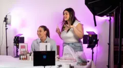 Dos mujeres venden productos frente a una cámara