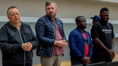 двое европейцев и двое африканцев стоят в наручниках