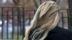 Alice de espalda, sentada en un banco en un parque