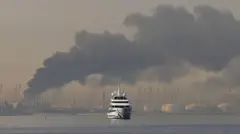 Iate navegando com uma coluna de fumaça se elevando do porto de Jebel Ali, após um ataque iraniano a Dubai, nos Emirados Árabes Unidos, no dia 1º de março de 2026