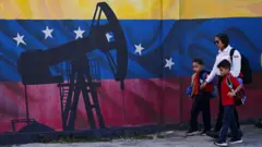 Una mujer con sus hijos pasea por un mural con balancín de petróleo y la bandera venezolana de fondo.