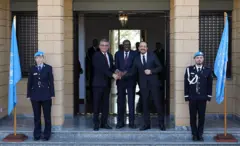 Kıbrıs'ın kuzeyindeki Türk yönetiminin lideri Tufan Erhürman (solda) ve Rum yönetiminin lideri Nikos Hristodulidis (sağda), BM Kıbrıs Temsilcisi Khassim Diagne eşliğinde bir araya geldi. Üç yetkili ellerini üst üste koymuş, kameralara gülümsüyor.