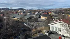 Várias casas e árvores na cidade de Kirkenes, com colinas cobertas de neve ao fundo