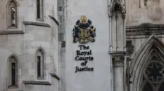 白いゴシック様式の建物にイギリスの国章が掲示され、その下に「The Royal Courts of Justice」と書かれている