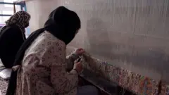 شابتان تجلسان أمام نول، لنسج سجادة كبيرة