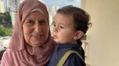 Senhora com véu islâmico e bebê no colo; ao fundo, prédios de São Paulo