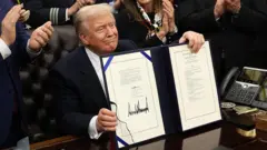 Donald Trump dey smile as e sign di spending bill into law wey go end di longest goment shutdown for di kontri history