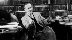 Tolkien sentado, conversando, com prateleirascasa das apostas netlivros ao fundo