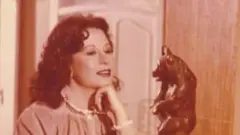 الفنانة الراحلة سمية الألفي أثناء أدائها لدور الأميرة نورهان في المسلسل المصري "ليالي الحلمية"، وتقف الألفي أمام تمثال، بينما ترتدي فستاناً طويلاً ذا أكمام طويلة وينساب شعرها الكثيف أسفل ظهرها، وتضع أحمر شفاة.