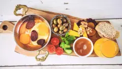 Travessa com frutas, azeitonas, pães, queijo, nozes, geleia e suco de laranja