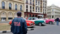 Una persona de espaldas con una chaqueta que dice USA en una calle en Cuba