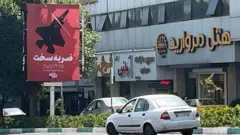 Um carro passa ao lado de um outdoor com os dizeres "Resposta Severa", em Teerã