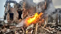 Зруйнований будинок і вогонь перед ним