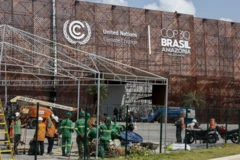Operários trabalhando em frente a grande centro de convenções com logomarcas da ONU e da COP30