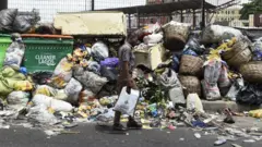 Aworan òketè idọti ati ẹnikan to n kọja niwaju rẹ