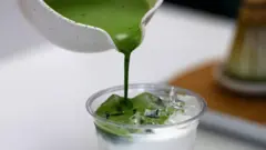 プラスチック容器に氷を浮かべた牛乳が入り、そこに上から別の白い容器に入った濃い目の抹茶が注がれている