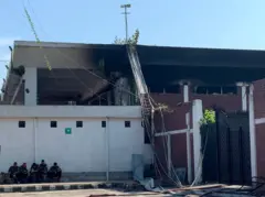 বিমানবন্দরের কার্গো ভিলেজে পুড়ে কালো হয়ে যাওয়া ভবনের ছাদ, ভবনটির সামনে বসে আছেন পাঁচ জন ফায়ার ফাইটার