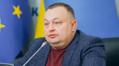 Олексій Антипович у бордовому светрі і картатому піджаку сидить за столом перед мікрофоном