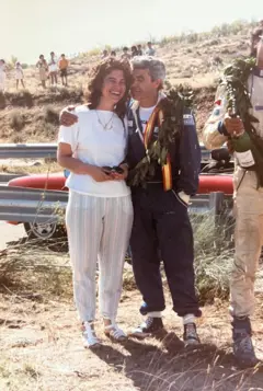 Juan López vitorioso, com uma medalha no peito e uma coroa de flores, abraça carinhosamente sua esposa, que sorri alegremente para a câmera