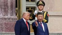 Çin lideri Trump'a bir yeri eliyle gösteriyor. Arkada esas duruşta bir çin askeri var.