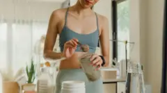 Uma mulher vestindo roupas de ginástica prepara uma bebida de colágeno com pó, água e leite