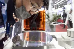 Um homem de óculos e máscara facial se curva para olhar para um wafer semicondutor circular