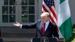 Trump stretch hand behind podium wit America and Nigeria flags behind am
