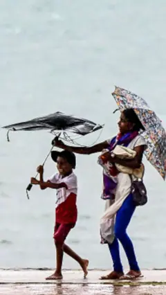 කාන්තාවක් සහ කුඩා පිරී දරුවෙක් වැස්ස අවස්ථාවක මුහුදක් අසලින් ගමන් කරන අතර දරුවාගේ කුඩය සුළඟට ගසා ගෙන යන අයුරු පෙනේ.