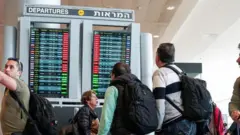 المسافرون ينظرون إلى شاشة تعرض الرحلات الجوية المتأخرة بعد تعليق الإقلاع كجزء من الاحتجاجات على مستوى البلاد ضد خطة الإصلاح القضائي للحكومة، وفقا لمتحدث باسم المطار (ليس في الصورة)، في مطار بن غوريون الدولي في اللد، إسرائيل في 27 مارس/آذار 2023