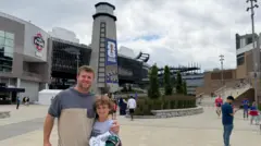 Eben Pingree segura um moletom preto na mão direita enquanto abraça o filho, Cole, em frente ao estádio de Boston