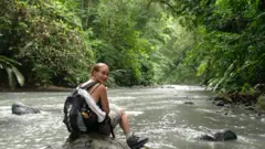 Una excursionistra con una mochila a cuestas descansa en una roca de un río en el Parque Nacional Corcovado