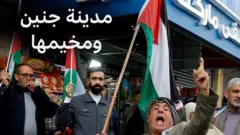 رجل فلسطيني يحمل العلم في مخيم جنين